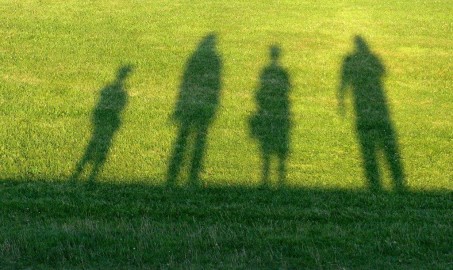 Auf diesem Bild sieht man Schatten von 4 Personen auf einer Wiese. Das Bild steht für die Oberbegriffe Patient:innen und Angehörige